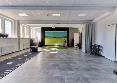 Bild des Trainingsraums vom Sport und Schmerz campus, links ein Laufband auf dem Boden, hinten der Golfsimulator
