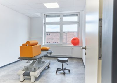 Physiotherapiepraxisraum von Physio mit Konzept in einem hellen Zimmer mit Liege, Ball, Nackenstützen etc. in orange